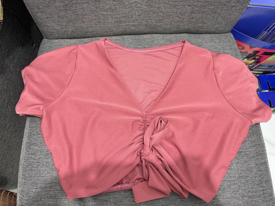 Pink V-Neck Crop Top (Category: Others Tops) located in Rodriguez. Submitted by prelovedbylalaine (Listing ID 1468928693, Image 2). Description: - Color: Dusty pink - Style: Casual crop top with short sleeves and deep V-neckline - Details: Center front ruched gathering with a tied knot - Fit: Stretchy elastic hem at the back for comfort - Fabric: Lightweight and breathable, perfect for pairing with high-waisted jeans or skirts.