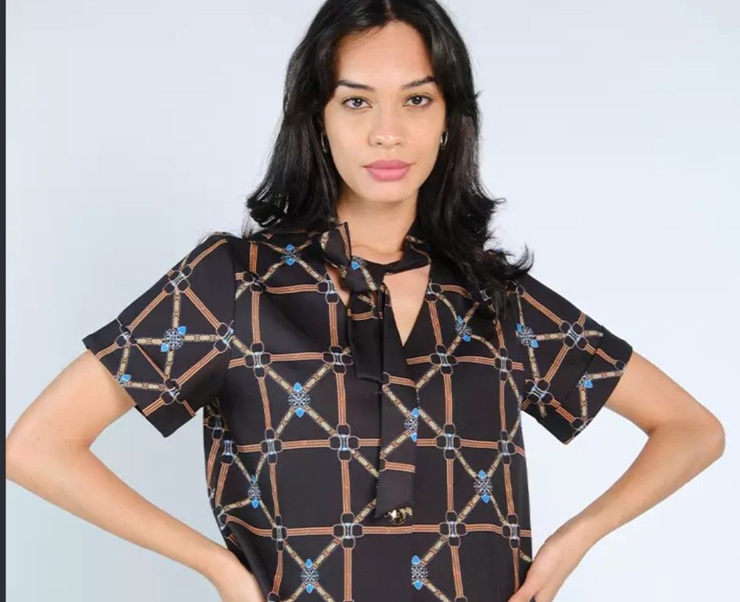 Plains and Prints Top (Category: Blouses) located in Iba. Submitted by geliqq (Listing ID 1468719888, Image 2). Description: - Style: Black short-sleeve blouse with chain and lattice pattern - Details: Cute neck tie at the collar - Fit: Relaxed and lightweight - Versatility: Easy to pair with skirts or trousers for work or casual wear - Condition: Clean and well-maintained.