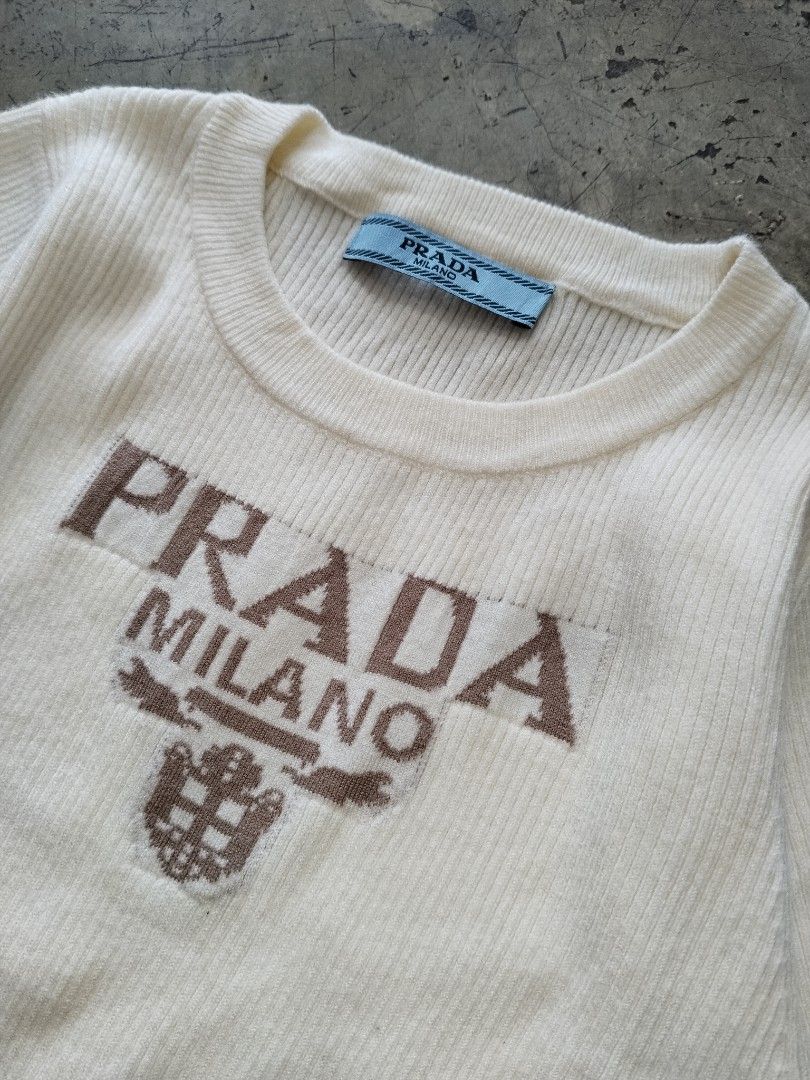 Prada Milano Knit T-Shirt White (Category: Shirts) located in Pasig City. Submitted by loveforlux_2025 (Listing ID 1468791467, Image 2). Description: - Color: White with brown Prada Milano knitted logo - Material: Soft, textured ribbed knit - Sleeves: Short sleeves - Neckline: Classic crew neck - Details: Authentic blue Prada brand label inside the collar.