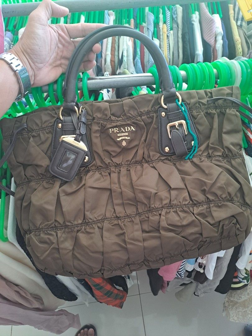 Prada Nylon Ruched Bag (Category: Luxury Bags & Wallets) located in Puerto Princesa. Submitted by jercksthriftph (Listing ID 1468928153, Image 1). Description: - Brand: Prada - Color: Rich brown - Material: Durable nylon with luxurious leather handles - Design: Stylish ruched exterior with iconic front logo plaque and matching leather key tag - Hardware: Elegant gold-tone accents - Interior: Signature Prada fabric lining with a convenient zippere