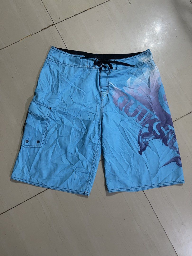 Quiksilver Blue Board Shorts Swim Trunks (Category: Swim Trunks & Board Shorts) located in Manila. Submitted by stuzzygod (Listing ID 1468856501, Image 1). Description: - Brand: Quiksilver -Size 34 - Length 22 - Leg open 12 - Color: Light blue with large purple smoke graphic print - Features: Single cargo pocket on the right leg with embroidered branding and eyelet drains - Waist: Drawstring waist closure with black lining - Origin: Made in Franc