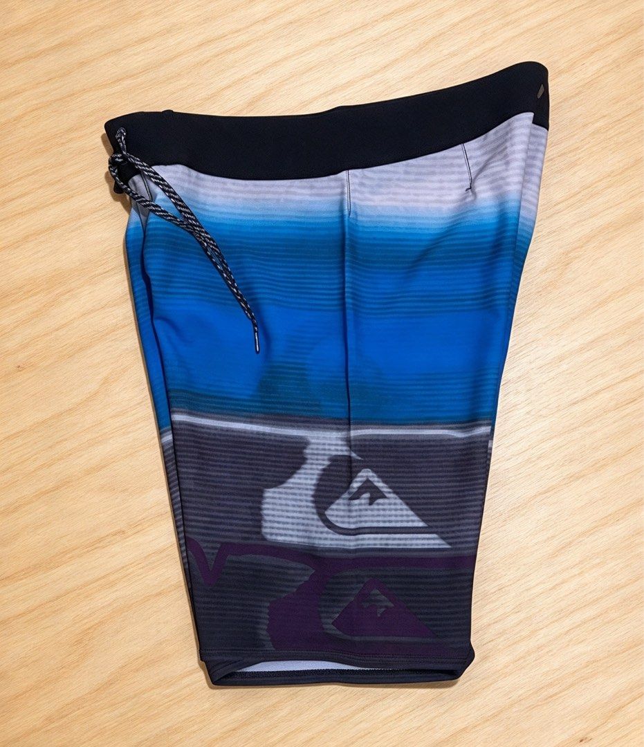 Quiksilver Blue Gradient Surf Board Shorts (Category: Swim Trunks & Board Shorts) located in Manila. Submitted by tygaangub1096 (Listing ID 1468884243, Image 2). Description: - Brand: Quiksilver - Size: 32 on tag 21 length - Design: Blue, grey, and purple gradient stripe pattern with a solid black waistband - Features: Braided black & white drawstring, single side pocket with flap and velcro closure - Branding: Quiksilver mountain & wave logo on 
