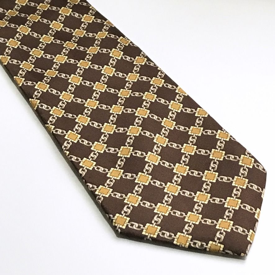 Rene Chagal Chain Link Pattern Brown Neck Tie (Category: Ties) located in Taguig. Submitted by retrogaze (Listing ID 1468774750, Image 2). Description: This vintage 100% silk handmade necktie by Rene Chagal features a deep chocolate brown base woven with a luminous satin twill finish. The body is decorated with an equestrian-inspired geometric grid pattern composed of interlocking silver-grey chain links joined by square ochre and mustard-gold li