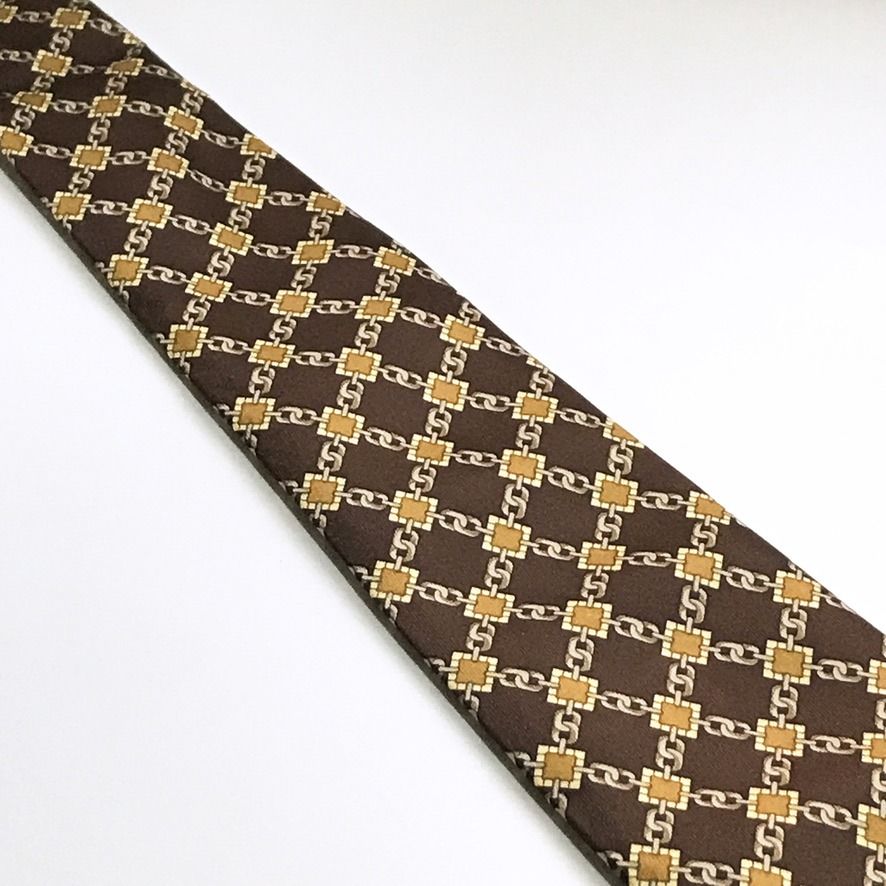Rene Chagal Chain Link Pattern Brown Neck Tie (Category: Ties) located in Taguig. Submitted by retrogaze (Listing ID 1468774750, Image 3). Description: This vintage 100% silk handmade necktie by Rene Chagal features a deep chocolate brown base woven with a luminous satin twill finish. The body is decorated with an equestrian-inspired geometric grid pattern composed of interlocking silver-grey chain links joined by square ochre and mustard-gold li