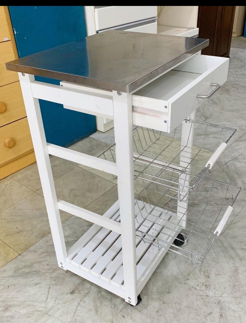 Rolling kitchen utility (Category: Bathroom & Kitchen Fixtures) located in Quezon City. Submitted by cmagday (Listing ID 1468802456, Image 2). Description: white rolling kitchen utility and serving trolley featuring a stainless steel top, a pull-out storage drawer, two wire metal vegetable baskets, a slatted bottom shelf, and caster wheels. material: White Wood & metal.