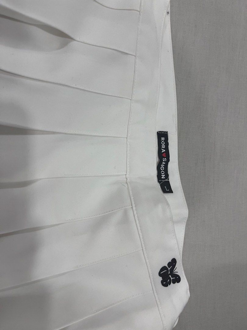 Rora Saigon white pleated skirt size L (Category: Skirts) located in Quezon City. Submitted by ashlymae (Listing ID 1468857189, Image 1). Description: - Brand: Rora Saigon - Size: L (tag attached inside waistband) - Color: Crisp white - Style: Classic pleated tennis skirt with side zipper and button fastening - Detail: Small black embroidered butterfly patch near the waist - Condition: Clean, minimal signs of wear.