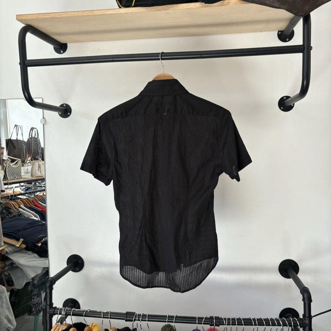 Semantic Design Black Short Sleeve Shirt Size L (Category: Shirts) located in Bambang. Submitted by heats777 (Listing ID 1468818104, Image 3). Description: - Brand/Model: Semantic Design - Color: Black with all-over vertical striped texture - Size: L (Regular fit) - Design Details: Front button closure, regular collar, and 'Dignified Heritage 64' graphic on the right chest - Extras: Includes replacement buttons attached to the inner tag - Conditi
