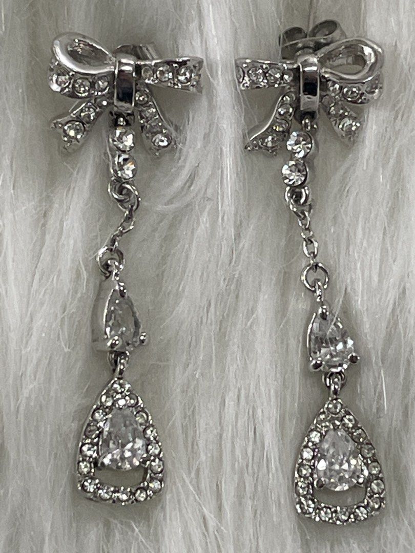 Silver Bow Rhinestone Drop Earrings (Category: Earrings) located in San Juan City. Submitted by redrosierose (Listing ID 1468716858, Image 2). Description: - Elegant silver dangle earrings with charming bow studs - Adorned with small rhinestone chains leading to a pear-shaped crystal drop - Catches the light beautifully for maximum sparkle - Secure post back closure - Ideal for weddings, parties, and dressed-up dinners RFS: Decluttering LOC: San 