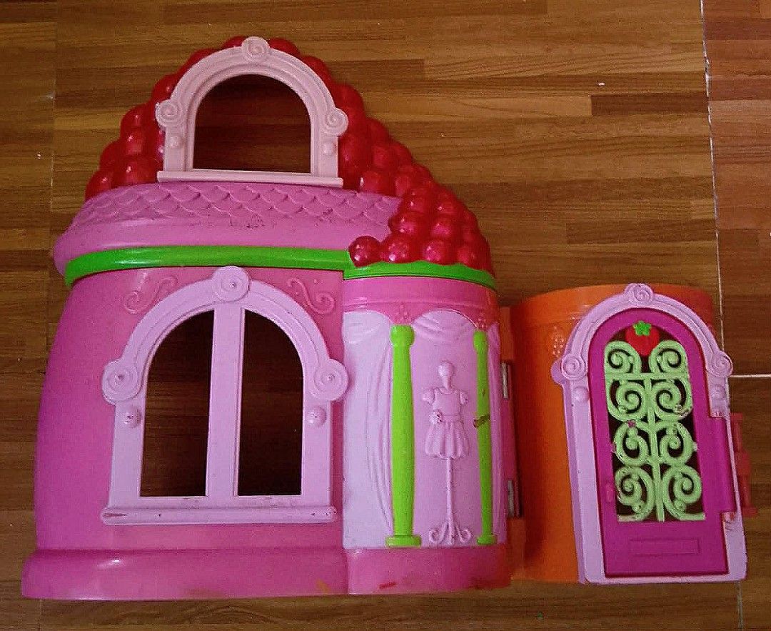 Strawberry Shortcake Dollhouse Playset (Category: Kids Toys) located in Paranaque City. Submitted by b_spilner (Listing ID 1468845868, Image 1). Description: - Strawberry Shortcake plastic dollhouse playset - Pink and red color scheme with green accents and strawberry-shaped roof - Opens to interior rooms with a mirror, shelves, and spinning display area - Door features decorative grillwork - Condition: Minor scuffs from previous use, overall stu