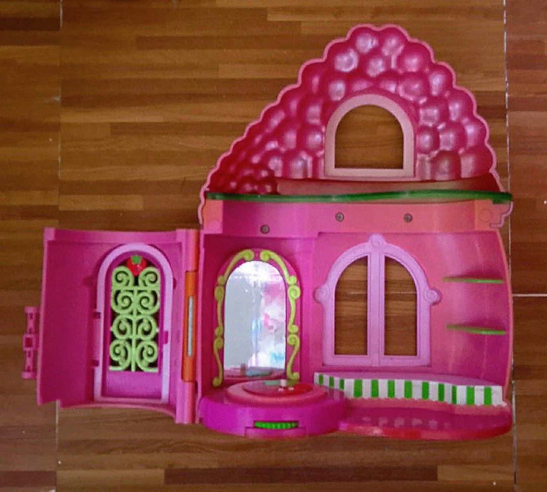 Strawberry Shortcake Dollhouse Playset (Category: Kids Toys) located in Paranaque City. Submitted by b_spilner (Listing ID 1468845868, Image 2). Description: - Strawberry Shortcake plastic dollhouse playset - Pink and red color scheme with green accents and strawberry-shaped roof - Opens to interior rooms with a mirror, shelves, and spinning display area - Door features decorative grillwork - Condition: Minor scuffs from previous use, overall stu