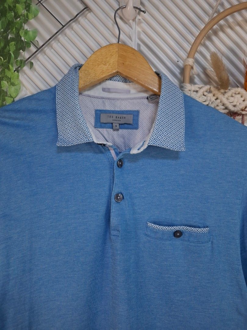 Ted Baker Blue Polo Shirt Medium (Category: Tshirts & Polo Shirts ) located in Bulacan. Submitted by cathycampo51092 (Listing ID 1468725987, Image 1). Description: Ted Baker blue polo shirt. Patterned collar and pocket trim. Chest width measures 21 inches, length is 27 inches. Fits like a Medium. Button placket at the front. Short sleeves. Clean fabric, well maintained..