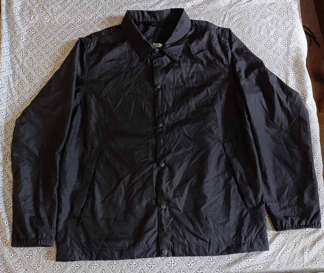 The North Face Black Coach Jacket Windbreaker (Category: Coats, Jackets and Outerwear) located in Cebu City. Submitted by jomeljakeg85353 (Listing ID 1468765216, Image 1). Description: - Brand: The North Face - Color: Solid black - Material: Lightweight nylon - Closure: Classic fold-down collar with front snap-button closure - Pockets: Two front hand pockets - Details: Elastic cuffs, straight hem, and subtle tonal logo on upper left chest - Style