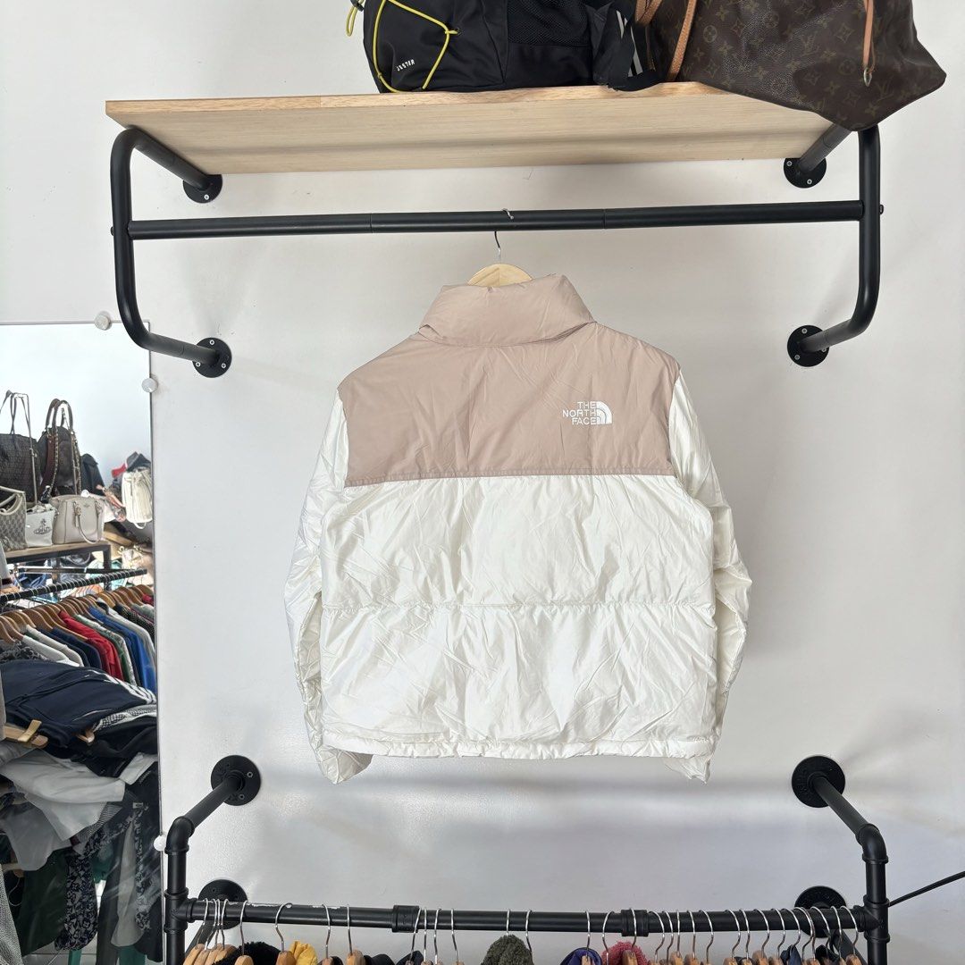 The North Face Puffer Jacket Beige White (Category: Coats, Jackets and Outerwear) located in Bambang. Submitted by heats777 (Listing ID 1468817841, Image 3). Description: - Brand: The North Face - Color: Beige and white colorblock - Features: Zip-up front, fleece-lined high collar, and durable YKK zippers - Details: Sleeve patch logo on the left arm with a quilted design on the lower white section and back - Condition: Excellent, warm winter oute