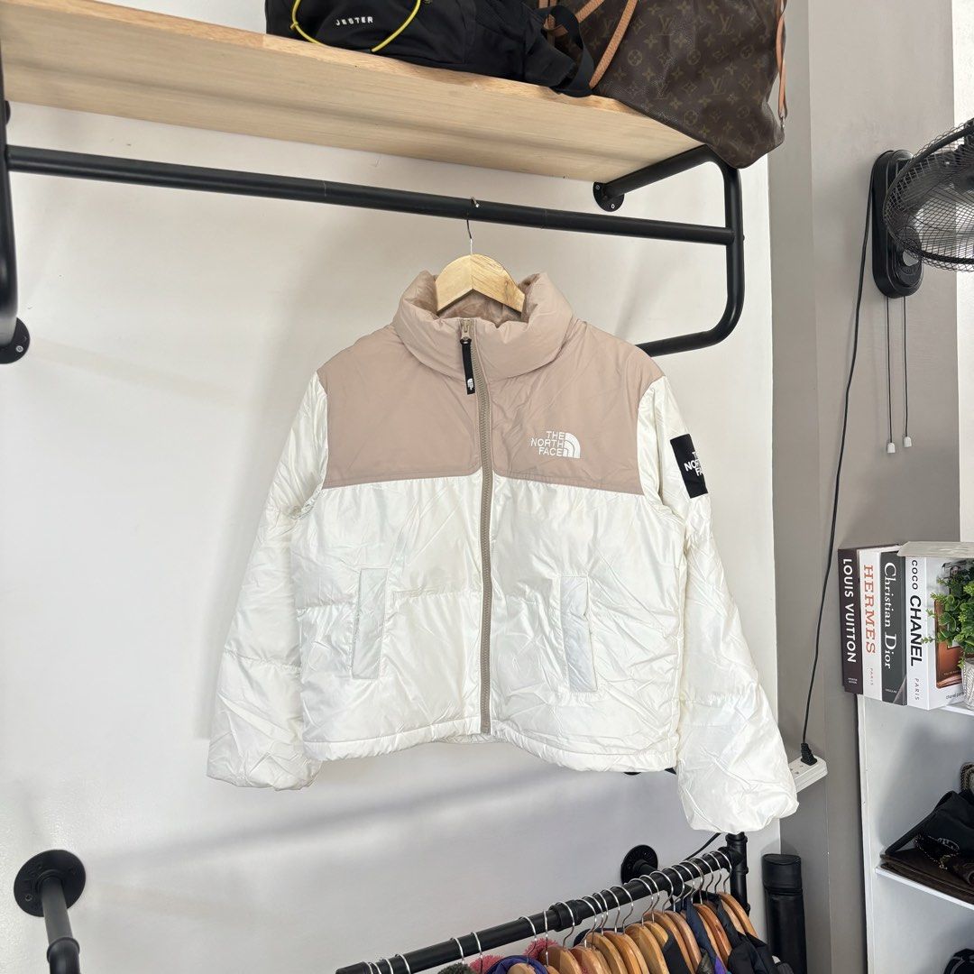 The North Face Puffer Jacket Beige White (Category: Coats, Jackets and Outerwear) located in Bambang. Submitted by heats777 (Listing ID 1468817841, Image 2). Description: - Brand: The North Face - Color: Beige and white colorblock - Features: Zip-up front, fleece-lined high collar, and durable YKK zippers - Details: Sleeve patch logo on the left arm with a quilted design on the lower white section and back - Condition: Excellent, warm winter oute