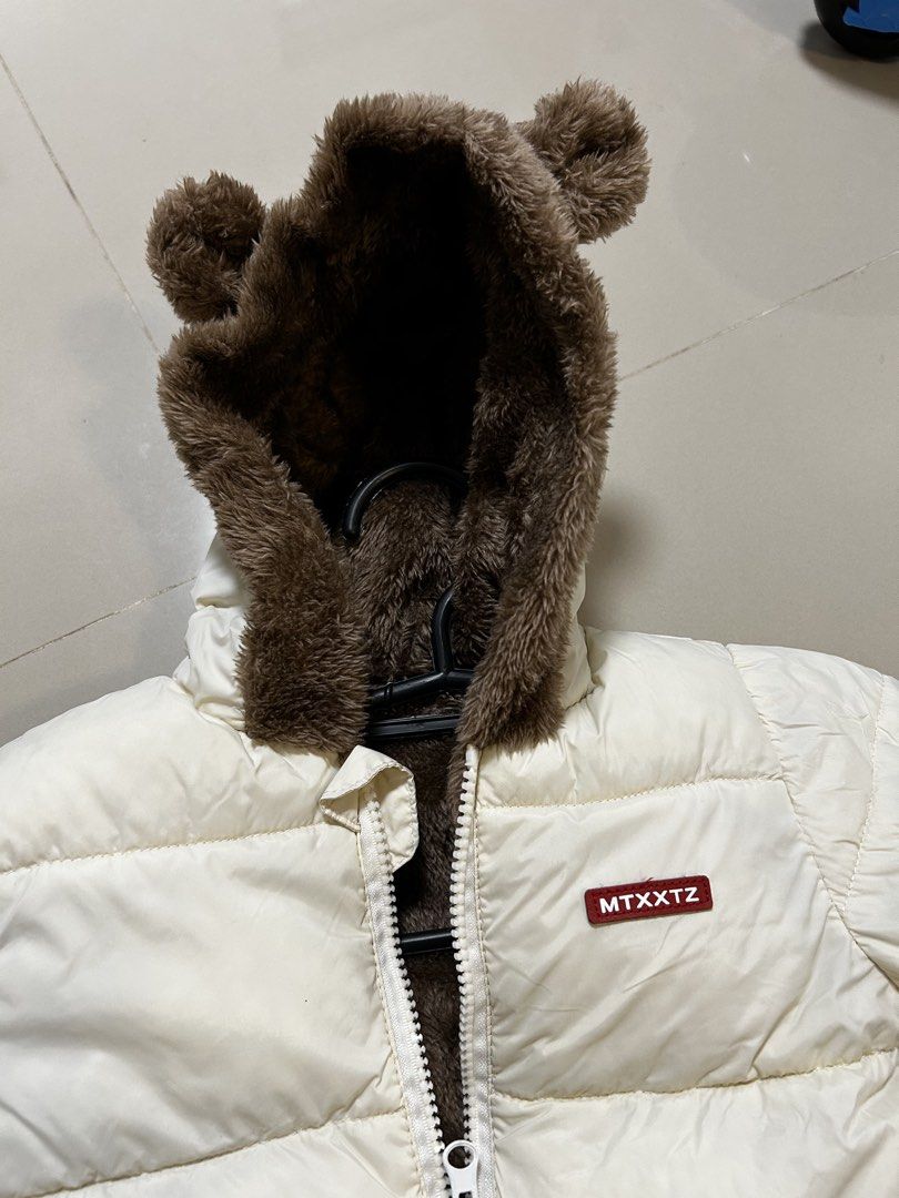 Toddler Puffer Jacket With Bear Ears (Category: Babies & Kids Fashion) located in Antipolo. Submitted by mommytj (Listing ID 1468741577, Image 2). Description: - Size: Toddler - Color: Off-white with brown furry lining - Features: Cute bear ears on hood, front zipper closure, two side pockets, and small red MTXXTZ chest patch - Condition: Worn once during our hongkong vacation, super cozy and warm - Perfect for cold weather and winter travels!.