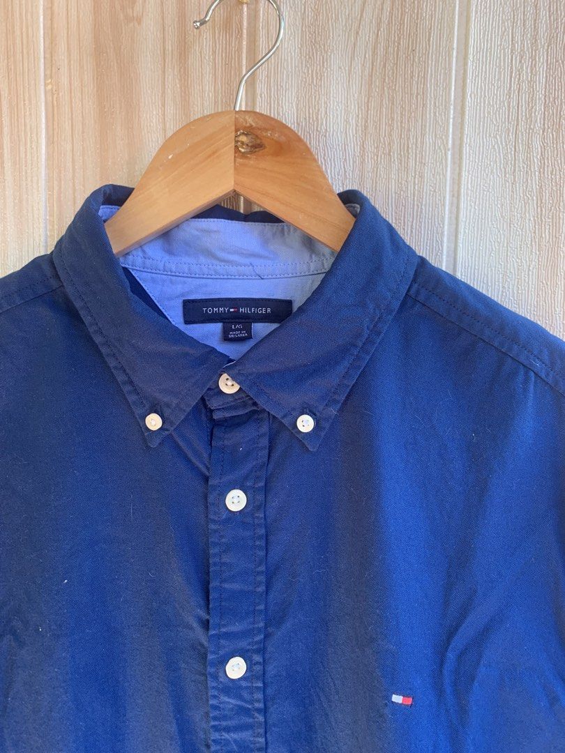 Tommy Hilfiger Blue Button-Down Long Sleeve Size L (Category: Tshirts & Polo Shirts ) located in Barobo. Submitted by pammythrift (Listing ID 1468752763, Image 3). Description: - Brand: Tommy Hilfiger - Color: Dark blue with contrasting light blue inner collar - Size: L (180/108B) - Material: 100% Cotton (Made in Sri Lanka) - Design: Classic button-down collar, front button closure, and embroidered flag logo on left chest - Condition: Clean, well