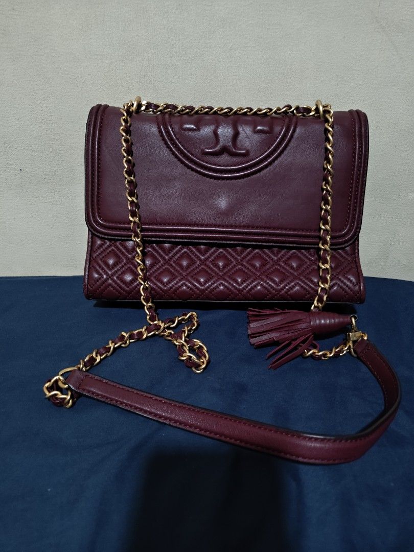 Tory Burch Burgundy Fleming Quilted Leather Shoulder Bag (Category: Luxury Bags & Wallets) located in Valenzuela. Submitted by wisewhale_46982b (Listing ID 1468768983, Image 1). Description: - Brand: Tory Burch - Color: Rich Burgundy - Material: Quilted leather body with smooth leather flap - Hardware: Gold-tone chain strap with leather shoulder guard - Details: Embossed T logo, matching tassel charm, and magnetic flap closure - Interior: Clean l