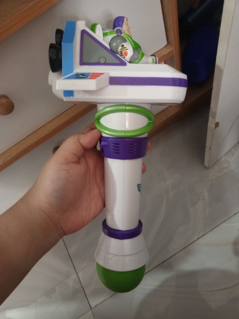 Toy Story Buzz Lightyear Bubble Blower Wand (Category: Action & Battle Toys) located in Manila. Submitted by iccythng0216 (Listing ID 1468741917, Image 2). Description: Buzz Lightyear bubble blower toy. White body with purple and green details. Features a bubble wand nozzle on the front with three red and yellow circular ports behind it. Action figure of Buzz Lightyear seated on top of the blaster unit. Handle has a purple power switch on the sid