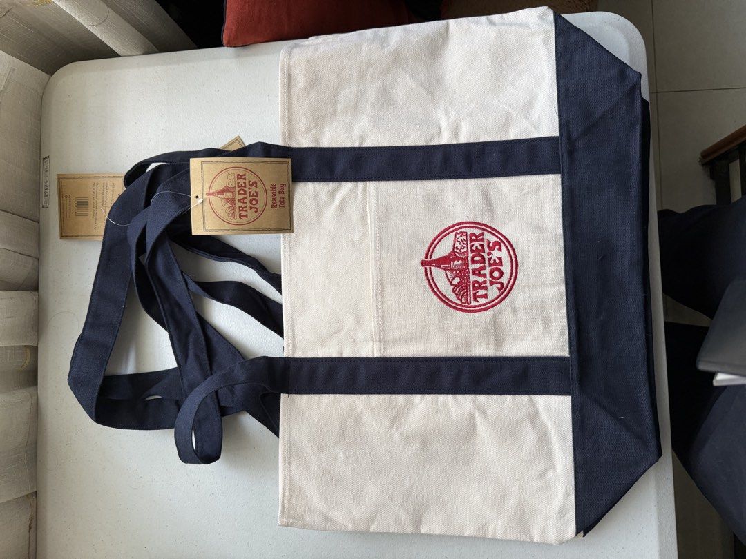 Trader Joe's Reusable Canvas Tote Bag Large (Category: Tote Bags) located in Manila. Submitted by richelann34088 (Listing ID 1468764299, Image 2). Description: - 100% Authentic Trader Joe's canvas tote bag - Large size with a spacious interior for all your everyday essentials - Stylish cream body paired with contrasting dark navy blue straps and bottom panel - Features a striking red embroidered Trader Joe's logo on the front pocket.