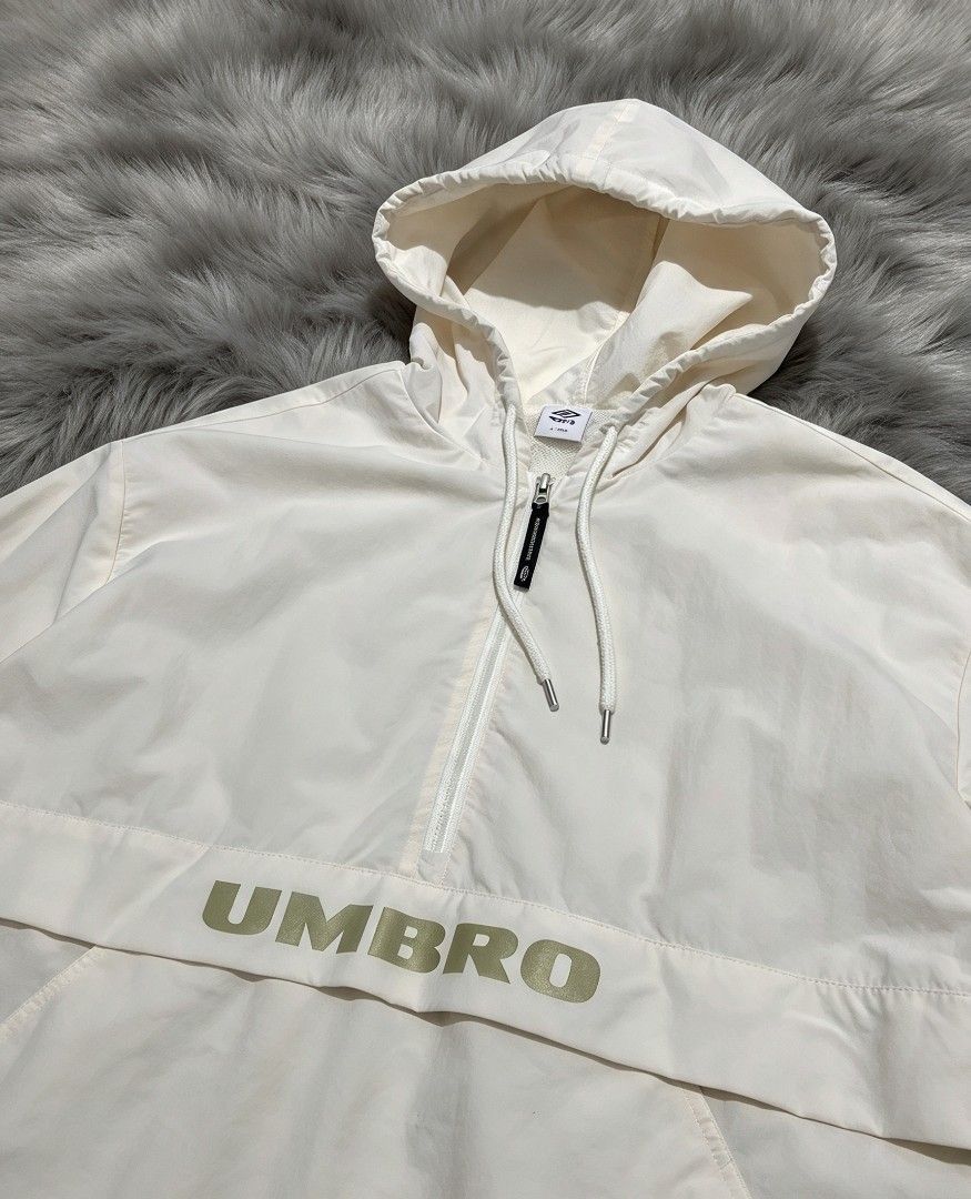Umbro White Half-Zip Hooded Windbreaker Jacket (Category: Coats, Jackets and Outerwear) located in Manila. Submitted by i_canthriftyoubetter8 (Listing ID 1468799148, Image 3). Description: - Brand: Umbro - Color: White with olive green branding - Features: Half-zip front closure, drawstring hood, kangaroo pocket - Fit: Elastic cuffs and hem - Material: Lightweight, ideal for layering on windy days - Condition: Clean overall.