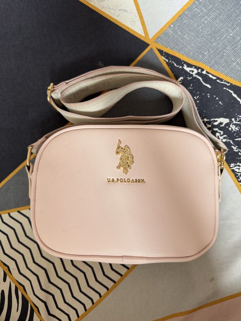U.S. Pink Sling Bag (Category: Cross-body Bags) located in Munoz. Submitted by shop.holiic (Listing ID 1468740350, Image 1). Description: - Brand: U.S. Polo Assn. - Style: Pink camera-style crossbody bag - Hardware: Gold-tone with embossed front logo - Strap: Wide, adjustable fabric strap with woven branding - Closure: Top zip closure - Interior: Lined with an open slip pocket - Condition: Clean, minimal signs of wear J&T MOP: Maribank/Gotyme/Gca