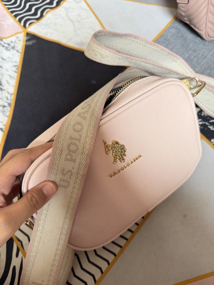 U.S. Pink Sling Bag (Category: Cross-body Bags) located in Munoz. Submitted by shop.holiic (Listing ID 1468740350, Image 2). Description: - Brand: U.S. Polo Assn. - Style: Pink camera-style crossbody bag - Hardware: Gold-tone with embossed front logo - Strap: Wide, adjustable fabric strap with woven branding - Closure: Top zip closure - Interior: Lined with an open slip pocket - Condition: Clean, minimal signs of wear J&T MOP: Maribank/Gotyme/Gca