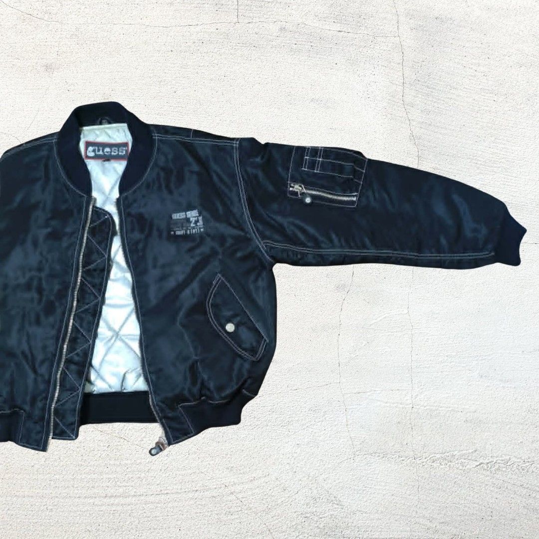 Vintage Guess Black Bomber Jacket with Quilted Lining (Category: Coats, Jackets and Outerwear) located in Baguio. Submitted by hevimetl (Listing ID 1468853529, Image 2). Description: - Brand: Guess - Color: Classic Black with contrasting white stitching - Interior: Quilted silver lining for extra warmth - Pockets: Dual side pockets and sleeve utility pocket - Details: Small chest graphic, bold Guess branding on the back, and ribbed collar, cuffs,