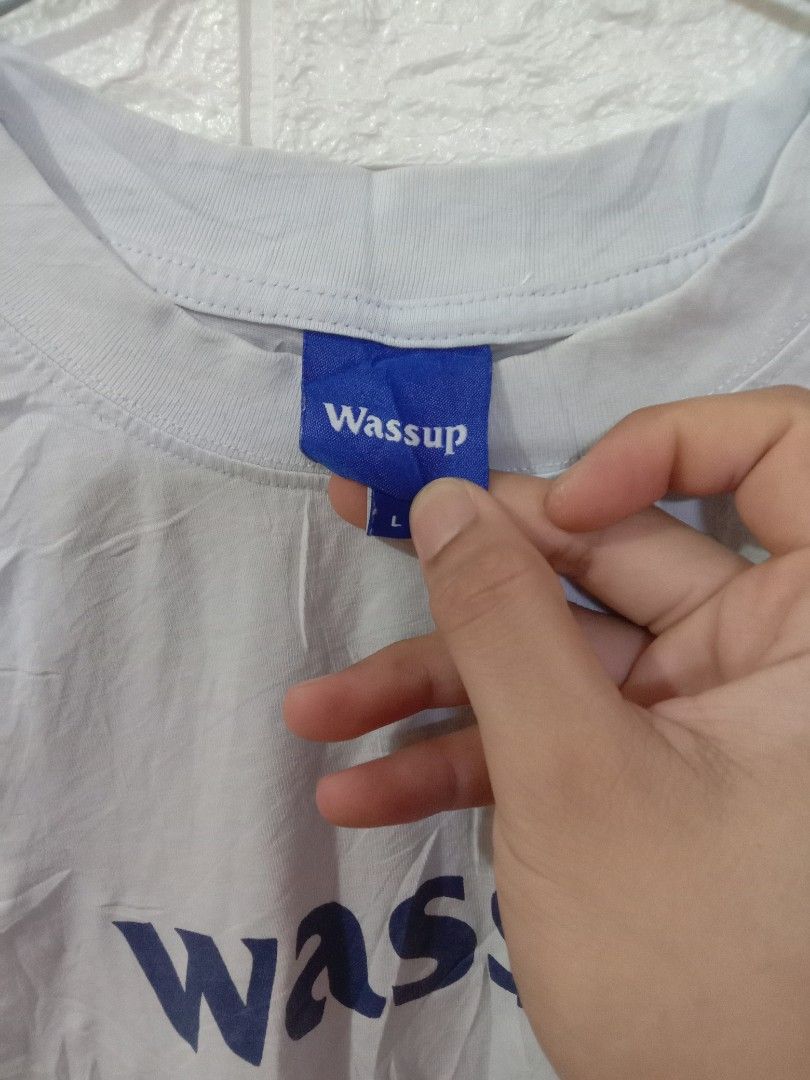 Wassup (Category: Tshirts & Polo Shirts ) located in Quezon City. Submitted by coolture_thriftph (Listing ID 1468755143, Image 3). Description: - Brand: DGCR Wassup - Color: Light blue with bold blue 'wassup' chest print - Size: L (neck tag attached) - Fit/Style: Short sleeves, crew neck - Details: Small blue brand tags on the collar and lower hem - Material/Care: Woven care label inside with washing instructions (Made in China) -Dimes 21w x 26 L