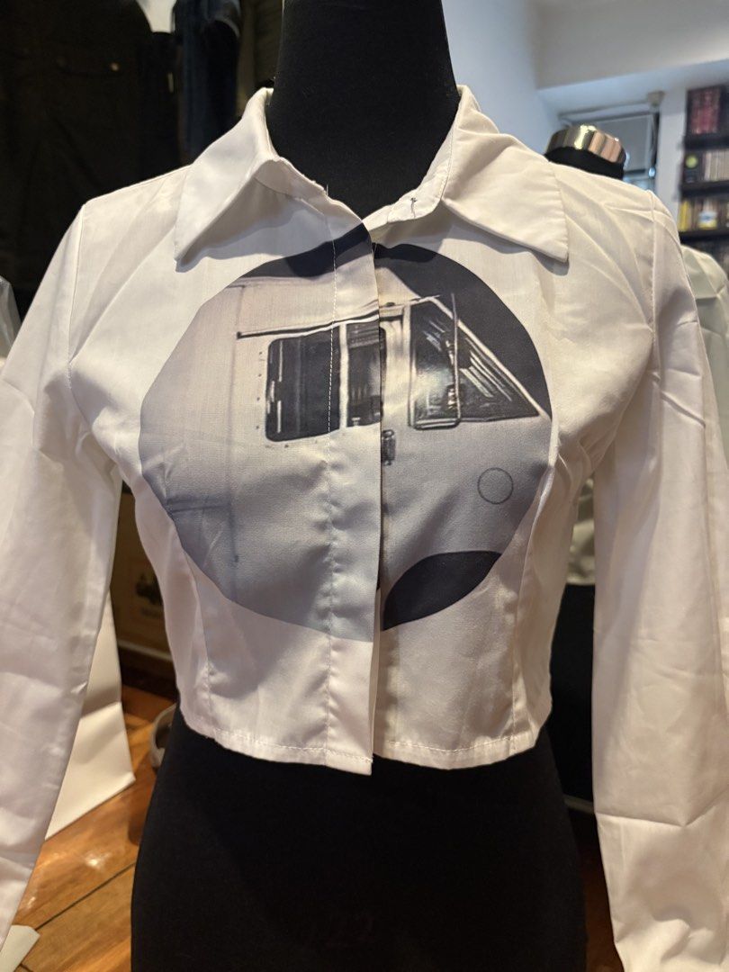 White Crop Top Button-Up Shirt With Graphic Print (Category: Shirts) located in Makati City. Submitted by audrey.hepburn (Listing ID 1468791837, Image 3). Description: - Style: Long-sleeve crop top button-up shirt - Design: Bold black and white vehicle graphic print across the chest - Details: Collared neckline, button-front closure, clean hem - Material: Crisp, structured cotton - Condition: Brand new / Excellent quality - Perfect for: Casual st