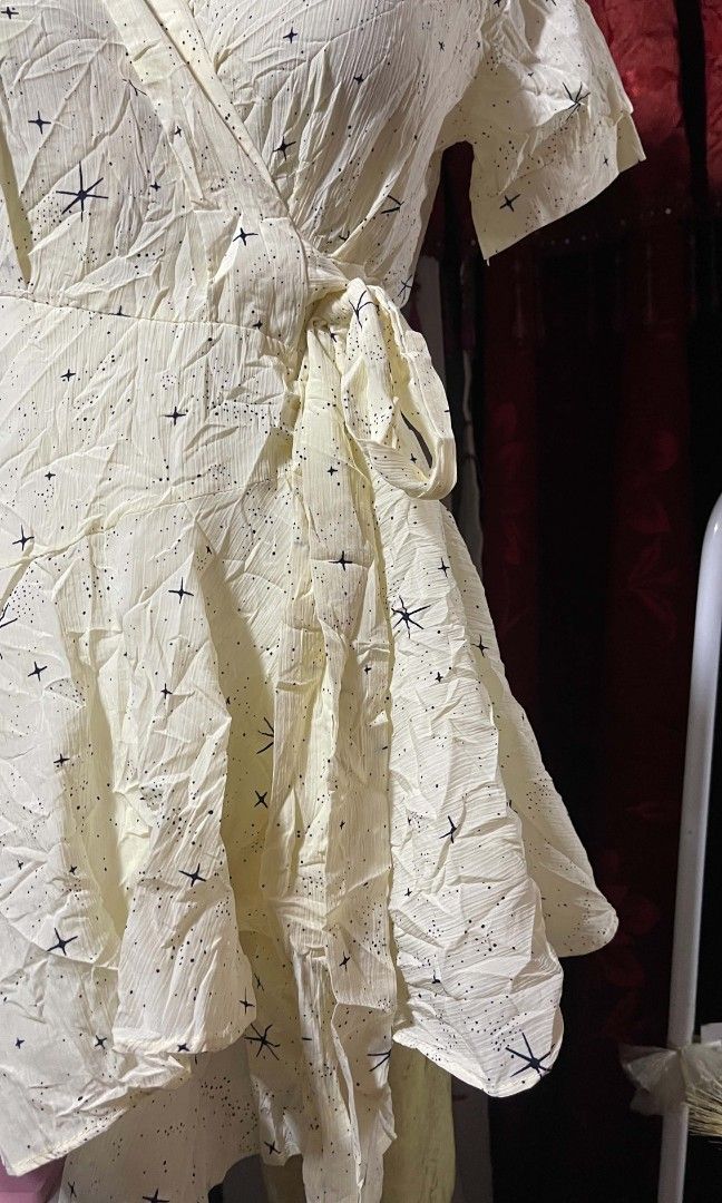 Wrap dress (Category: Dresses) located in Manila. Submitted by wheneity67thifted (Listing ID 1468927429, Image 3). Description: The image shows a cream-colored, short-sleeve wrap dress or crossover mini dress adorned with a subtle star-like pattern and a side-tie waist..