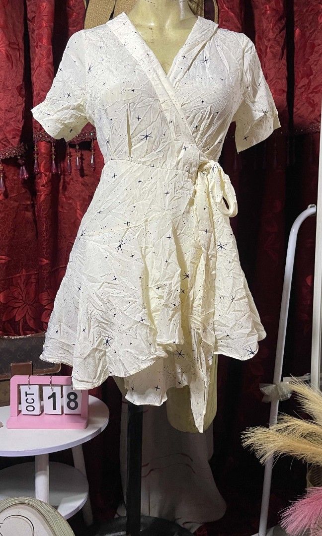 Wrap dress (Category: Dresses) located in Manila. Submitted by wheneity67thifted (Listing ID 1468927429, Image 2). Description: The image shows a cream-colored, short-sleeve wrap dress or crossover mini dress adorned with a subtle star-like pattern and a side-tie waist..