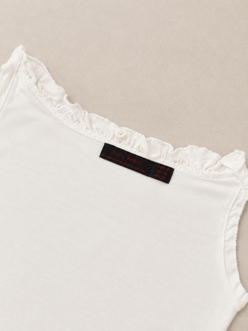 Zara Basic White Ruffled Tank Top Size M (Category: Sleeveless) located in Manila. Submitted by lexiandco.ph (Listing ID 1468721901, Image 2). Description: - Brand: Zara - Style: Basic tank top with scoop neckline and delicate ruffle trim - Color: White - Size: Medium (true to size) - Material: Soft and breathable cotton - Condition/Features: Versatile, great for layering or standalone wear in warmer weather.