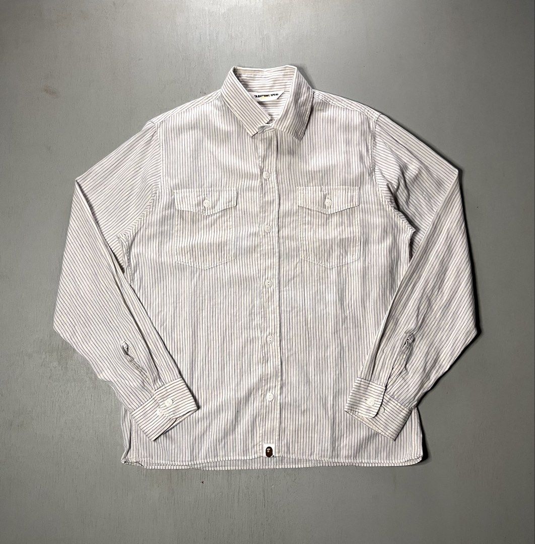 A Bathing Ape BAPE Blue Stripe (authentic) (Category: Tshirts & Polo Shirts ) located in Catbalogan. Submitted by yellfindss (Listing ID 1469131524, Image 2). Description: - 100% Authentic BAPE button-down shirt - Design: White fabric with fine blue vertical stripes -20.5/27 - Material: Lightweight and breathable 86% cotton, 14% linen blend - Origin: Made in Japan by Nowhere Co. - Details: Standard inner wash tags with gold ape head logo attached