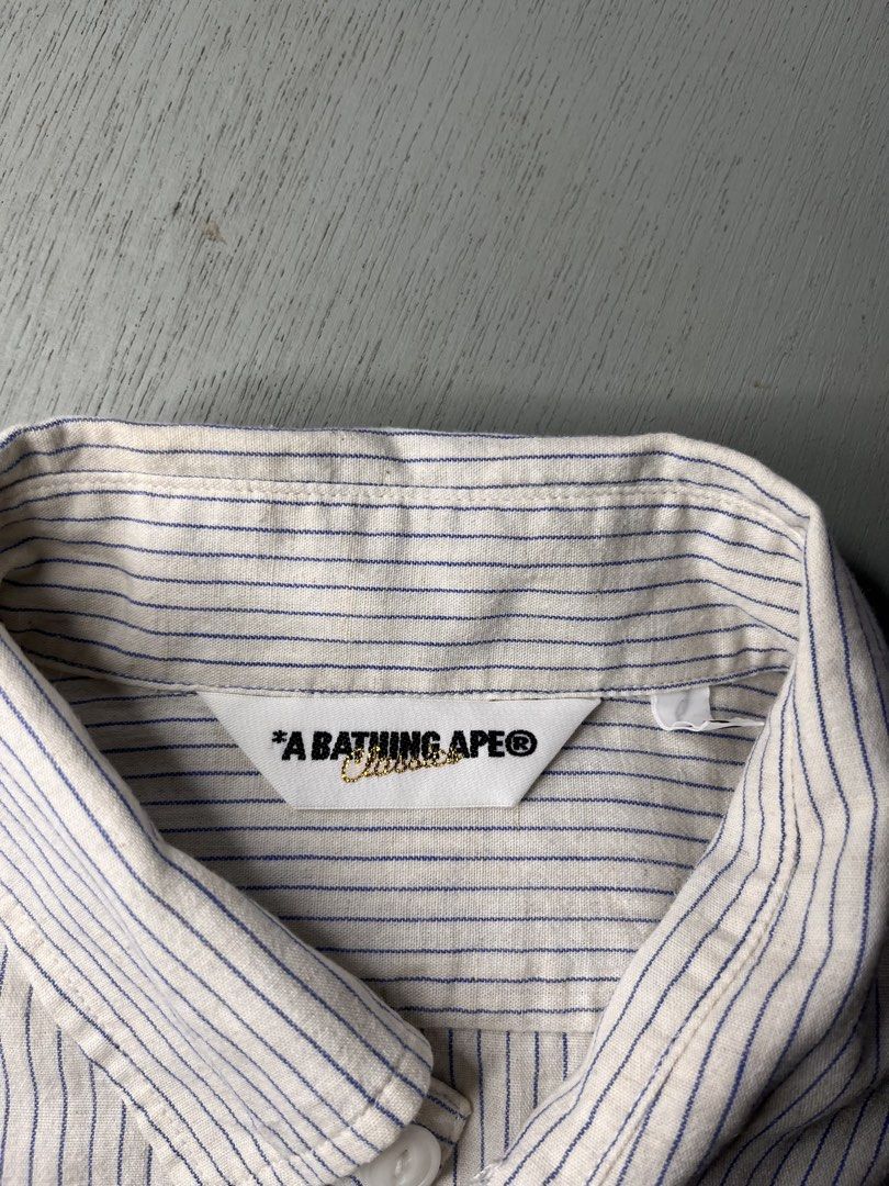 A Bathing Ape BAPE Blue Stripe (authentic) (Category: Tshirts & Polo Shirts ) located in Catbalogan. Submitted by yellfindss (Listing ID 1469131524, Image 3). Description: - 100% Authentic BAPE button-down shirt - Design: White fabric with fine blue vertical stripes -20.5/27 - Material: Lightweight and breathable 86% cotton, 14% linen blend - Origin: Made in Japan by Nowhere Co. - Details: Standard inner wash tags with gold ape head logo attached