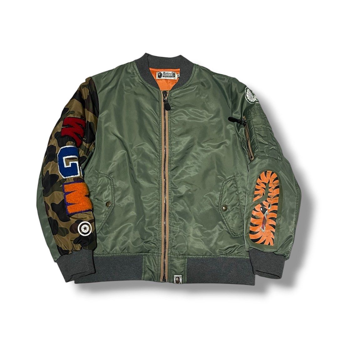 A Bathing Ape Shark Bomber Jacket Green Camo (Category: Coats, Jackets and Outerwear) located in Manila. Submitted by jstash09 (Listing ID 1468936094, Image 1). Description: - Brand: BAPE (A Bathing Ape) - Color: Sage Green with vibrant orange inner lining - Design: Classic shark face patch on the back - Sleeves: One camouflage sleeve with colorful chenille lettering, one tiger stripe patch sleeve -21 x 25 - Details: Ribbed grey collar, cuffs, an