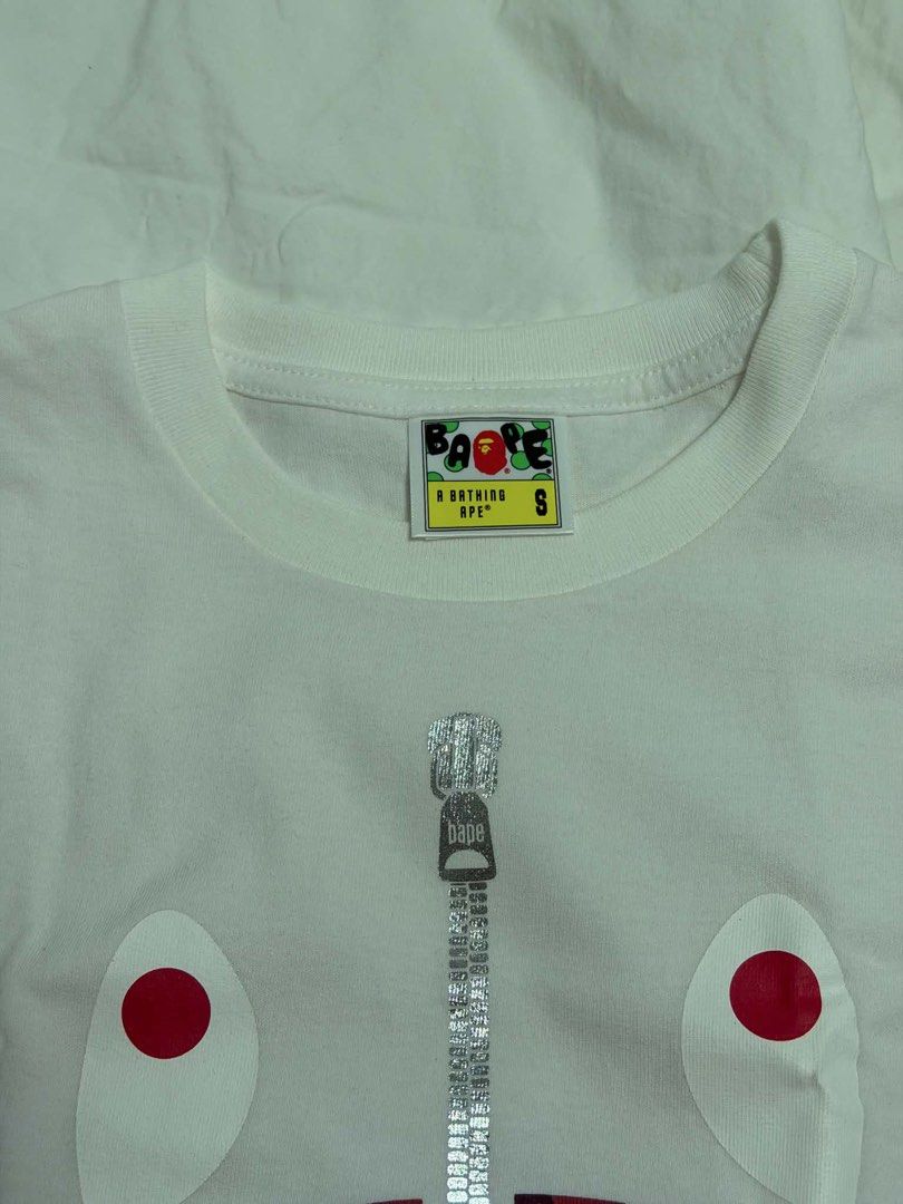 A Bathing Ape Shark Zip Graphic T-Shirt (Category: Tshirts & Polo Shirts ) located in Paranaque City. Submitted by gongonpo (Listing ID 1469003200, Image 2). Description: - Brand: A Bathing Ape (BAPE) - Color: White - Size: S (tag at neck) - Material: 100% cotton - Design: Iconic shark mouth and zipper print on front with red eyes - Authenticity: Includes Nowhere Co., Ltd wash tag - Condition: Clean fabric with clear prints on both sides.