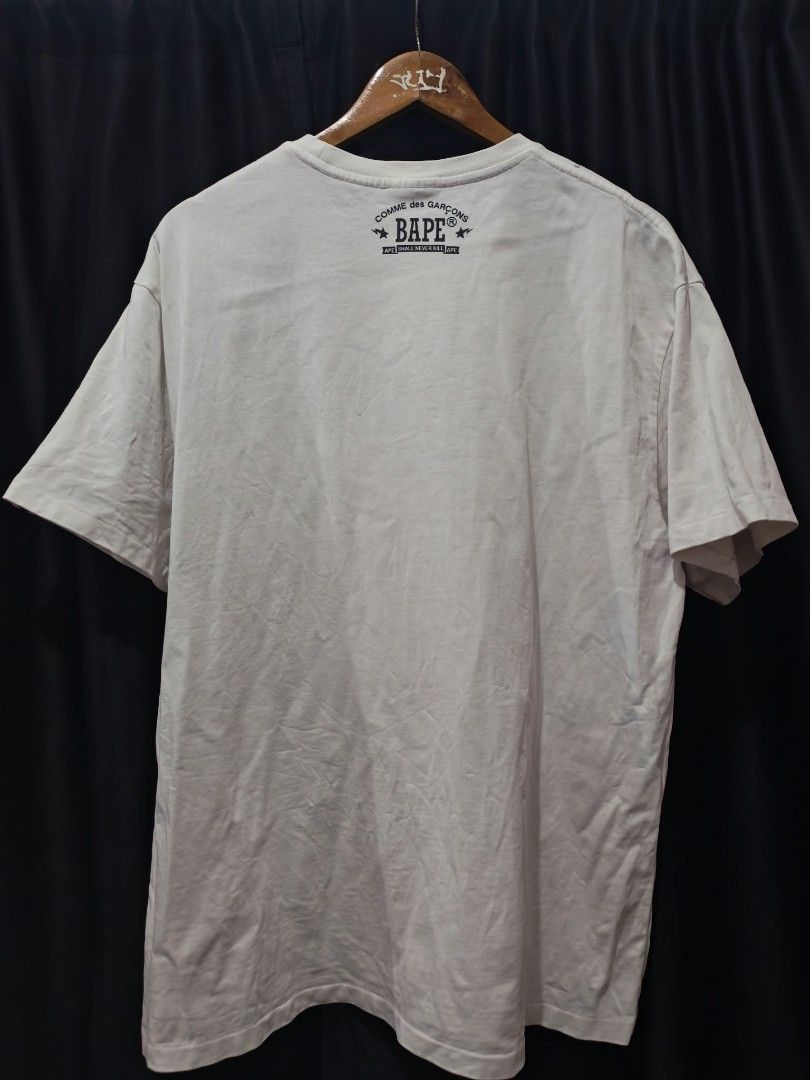 A Bathing Ape x Comme des Garcons T-shirt (Category: Shirts) located in Baguio. Submitted by solo_ukay (Listing ID 1469037984, Image 2). Description: - Authentic BAPE x Comme des Garcons collaboration - Color: Classic White - Material: 100% Premium Cotton (Regular fit, crew neck) - Design: Necklace and pendant graphic print on chest, bold lettering on back collar - Signature details: Small Ape head tag on left sleeve - Condition: Excellent / Well