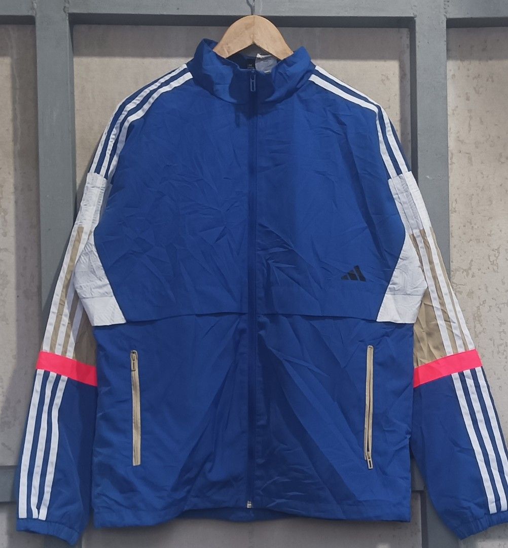 Adidas Blue Windbreaker Jacket (Category: Coats, Jackets and Outerwear) located in Muntinlupa City. Submitted by thriftben (Listing ID 1468930546, Image 1). Description: Blue Adidas windbreaker with white and tan stripes down the sleeves. Bright pink accent line near the cuffs. Full zip closure with zipped side pockets. Stand-up collar. Inner mesh lining. 100% recycled polyester construction. Made in China. Standard men's size M..