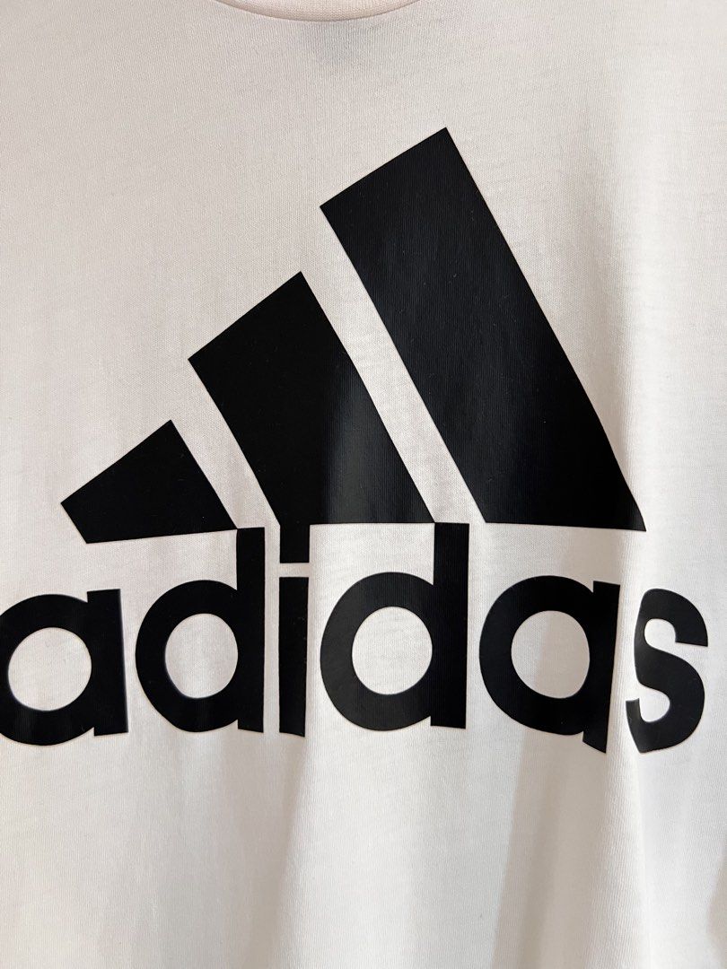 Adidas Essential Logo Tee in White/Black (Category: Activewear) located in Imus. Submitted by prelovedfinds84 (Listing ID 1468993630, Image 3). Description: This classic, regular-fit athletic t-shirt is crafted from 100% cotton single jersey fabric for a soft and comfortable feel. It features a traditional crewneck collar, short sleeves, and prominently displays the signature adidas Badge of Sport logo printed in black across the chest..