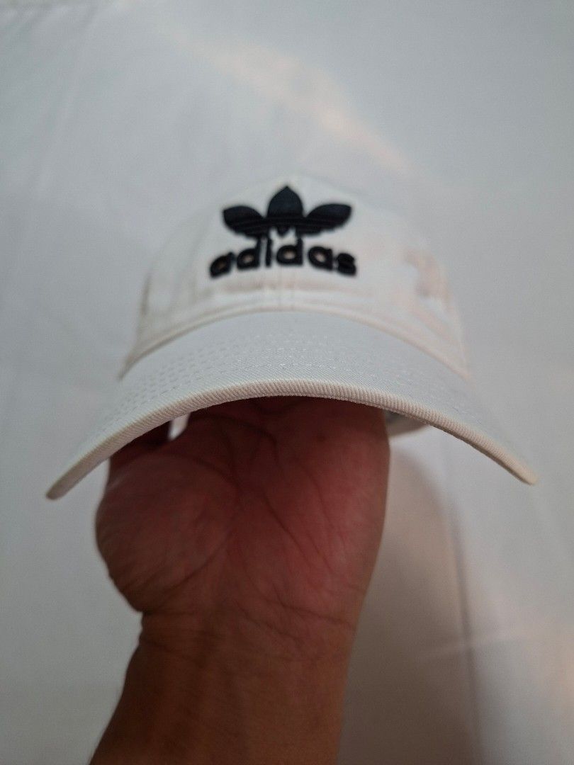 Adidas White Trefoil Baseball Cap (Category: Caps & Hats) located in Baguio. Submitted by restyrille77846 (Listing ID 1469065652, Image 2). Description: - Authentic Adidas baseball cap in classic white - Features iconic embroidered black trefoil logo on the front - Adjustable back strap with white metal buckle and subtle branding - Built-in ventilation eyelets for all-day breathability - Versatile design that matches any casual outfit.