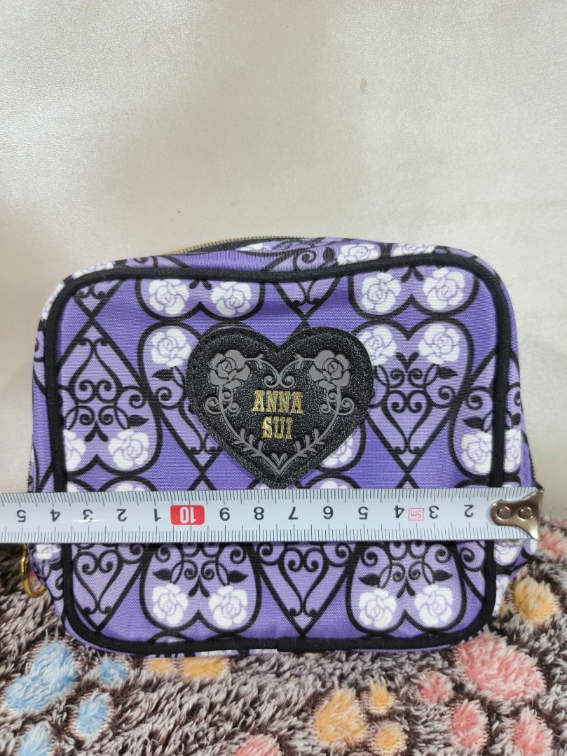 Anna Sui Purple Rose Pattern Cosmetic Pouch (Category: Purses & Pouches) located in San Leonardo. Submitted by burgossanleonardo.12345 (Listing ID 1469078072, Image 2). Description: - Brand: Anna Sui - Design: Purple with black filigree and white rose pattern - Front Detail: Black heart-shaped patch with gold glitter Anna Sui logo - Hardware: Gold zipper with a chic round pull ring - Interior: Solid purple lining with multiple slip pockets and co