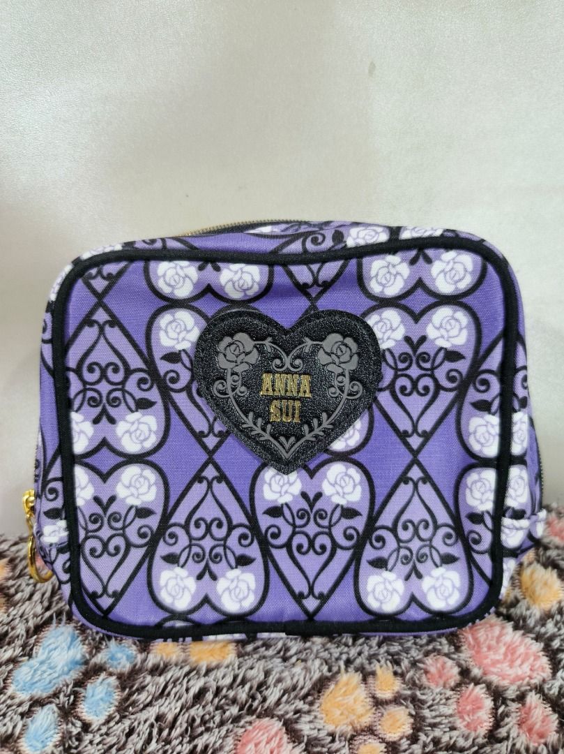Anna Sui Purple Rose Pattern Cosmetic Pouch (Category: Purses & Pouches) located in San Leonardo. Submitted by burgossanleonardo.12345 (Listing ID 1469078072, Image 1). Description: - Brand: Anna Sui - Design: Purple with black filigree and white rose pattern - Front Detail: Black heart-shaped patch with gold glitter Anna Sui logo - Hardware: Gold zipper with a chic round pull ring - Interior: Solid purple lining with multiple slip pockets and co