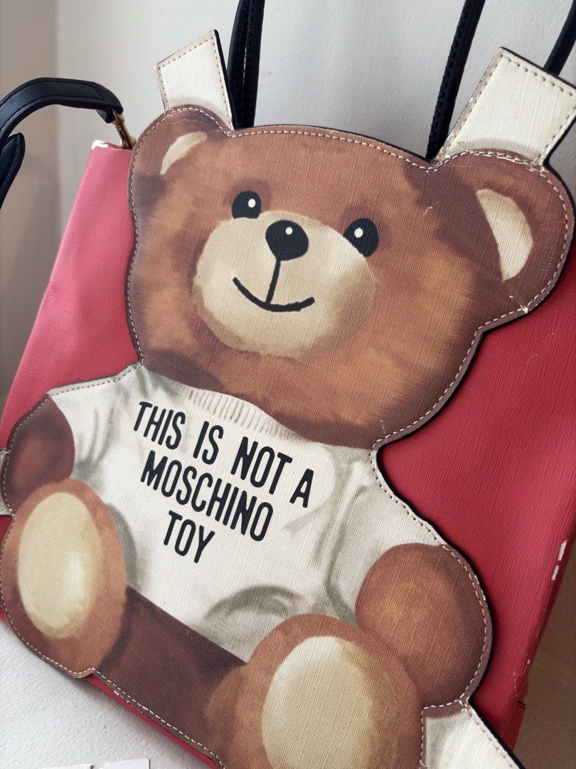 Authentic Moschino Shopping Bag Ready To Bear Tote (Category: Luxury Bags & Wallets) located in Mandaluyong City. Submitted by wear_your_style (Listing ID 1468962104, Image 2). Description: Bought for HKD 7,900 or ₱60K+ long time ago. Material is PU, parang PVC na malambot. Tag says color Red pero di siya yung nakakasilaw na red. Very roomy! Inside lining is nylon, malinis naman, with secret zipped pocket. Open tote po to na may snap buttons sa g