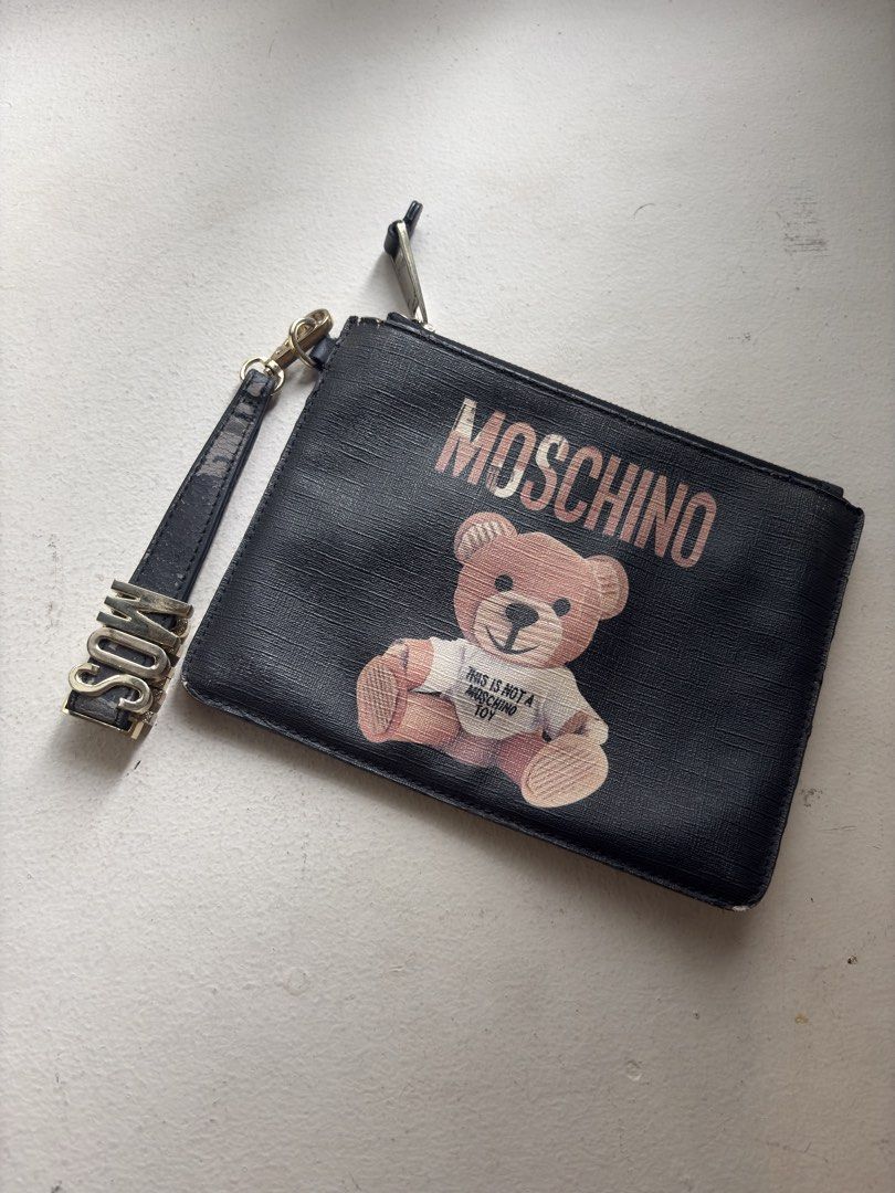 Authentic Moschino Teddy Bear Flat Clutch with Wristlet (Category: Luxury Bags & Wallets) located in Mandaluyong City. Submitted by wear_your_style (Listing ID 1468967946, Image 1). Description: Super nice. This the Couture line of Moschino, the most expensive line. Material is PU or PVC. Malambot naman siya. Inside lining is cloth with 1 zipped secret pocket. Black pa naman. The Teddy Bear is painted on the surface. Approx 9 inches wide and 7.5 