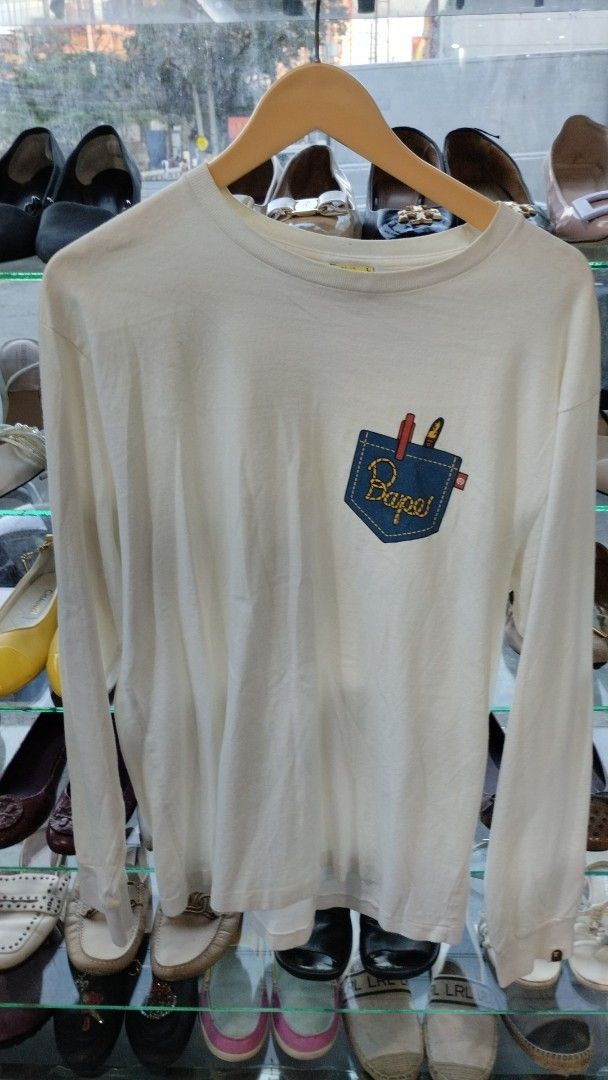 BAPE White Long Sleeve Pocket Graphic Tee (Category: Tshirts & Polo Shirts ) located in Manila. Submitted by niggzreyno51476 (Listing ID 1469026743, Image 1). Description: - Brand: BAPE (A Bathing Ape) - Style: White long sleeve shirt - Origin: Made in Japan - Material: 100% premium cotton - Design: Blue chest pocket graphic with pen and lighter - Details: Classic ape head logo tag on sleeve cuff, ribbed collar and cuffs - Perfect for streetwear 