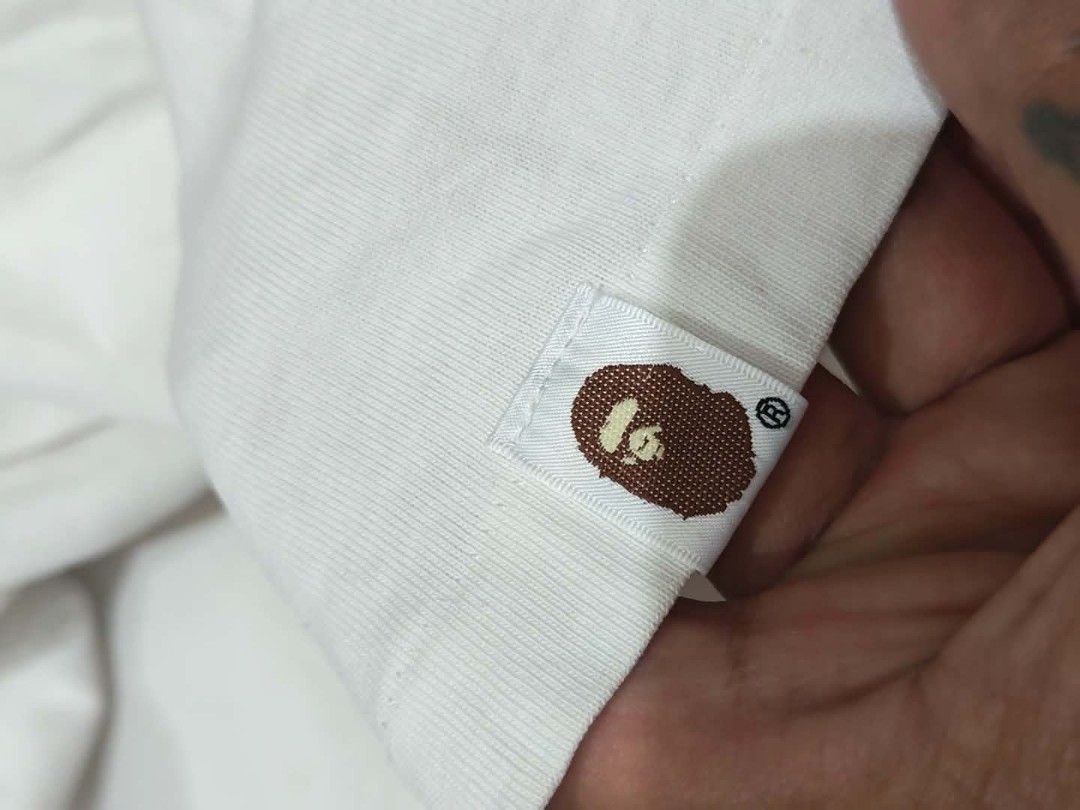 BAPE x COMME des GARÇONS White Tee (Category: Shirts) located in Baguio. Submitted by solo_ukay (Listing ID 1469038278, Image 3). Description: - Authentic BAPE x COMME des GARÇONS collaboration t-shirt in white - Eye-catching front graphic with multiple ape head prints and bold typography - Subtle co-branded text detail on the back collar - Signature sleeve tag stitched on the left cuff - Premium 100% cotton material, Made in Japan - Interior nec