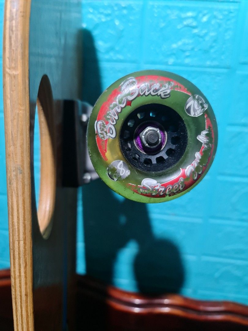 Bare Back Skateboard with Green Wheels (Category: Skates, Rollerblades & Scooters) located in San Mateo. Submitted by gk2900504184839 (Listing ID 1468936498, Image 3). Description: - Brand: Bare Back complete skateboard (ready to ride) - Deck: Wooden deck with center wood stripe and black grip tape on top - Design: Blue graphic logo on a natural wood finish bottom - Hardware: Green wheels with black hubs and stylish purple bushings - Condition: M