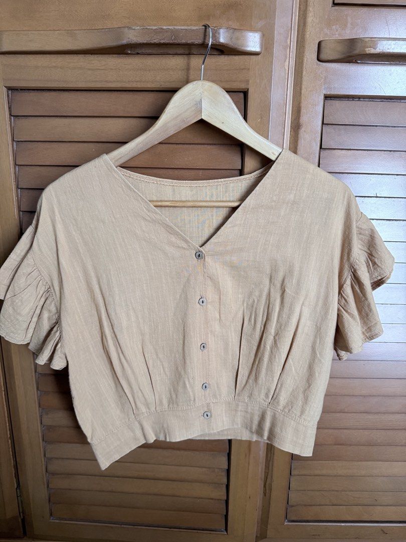 Beige V-Neck Crop Top with Ruffle Sleeves (Category: Sleeveless) located in Paranaque City. Submitted by roanclauds (Listing ID 1468957451, Image 1). Description: - Color: Beige - Style: Button-down crop top with V-neckline - Sleeves: Short ruffle sleeves - Fabric: Lightweight, textured linen-like material - Details: Wide waistband panel, plain back with gathered hem - Condition: Clean finish, ready to wear.