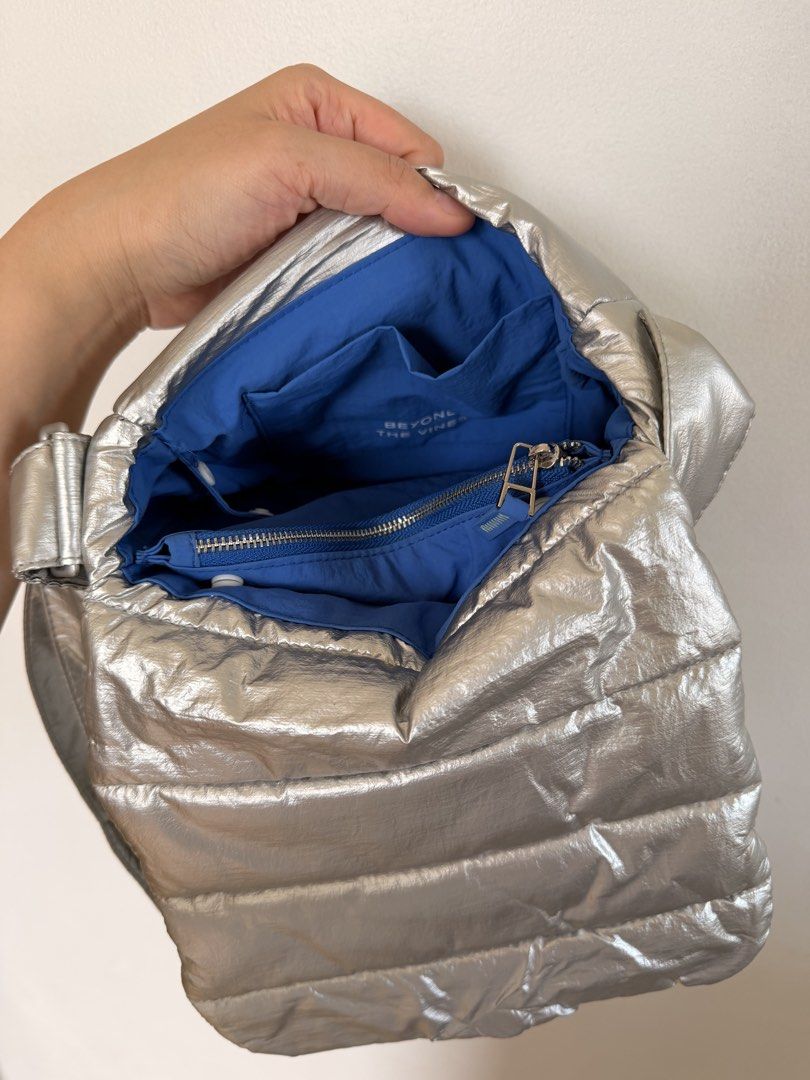 Beyond The Vines Silver Puffer Crossbody Bag (Category: Cross-body Bags) located in Marikina City. Submitted by melsellstuff (Listing ID 1468947515, Image 2). Description: - Brand: Beyond The Vines - Color: Metallic silver with vibrant blue interior lining - Design: Padded quilted puffer style with a small debossed logo patch - Straps: Thick and adjustable crossbody strap - Storage: Interior slip pockets and zippered compartment - Condition: Clea