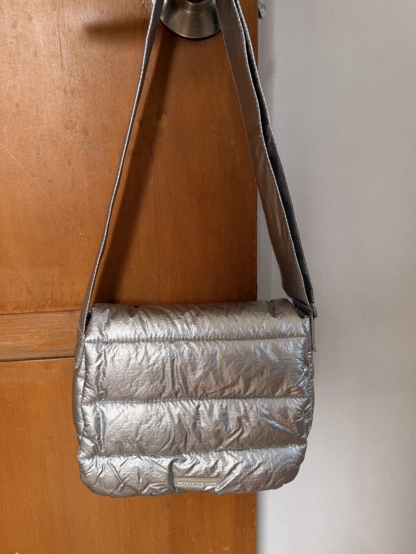 Beyond The Vines Silver Puffer Crossbody Bag (Category: Cross-body Bags) located in Marikina City. Submitted by melsellstuff (Listing ID 1468947515, Image 1). Description: - Brand: Beyond The Vines - Color: Metallic silver with vibrant blue interior lining - Design: Padded quilted puffer style with a small debossed logo patch - Straps: Thick and adjustable crossbody strap - Storage: Interior slip pockets and zippered compartment - Condition: Clea